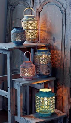 three lit lanterns sitting on top of a wooden shelf next to an old wood door