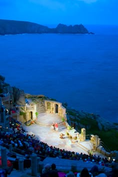 an outdoor theater with people sitting on the stage and looking out over the water at night