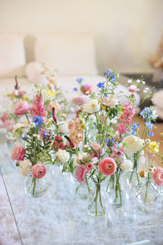 A Picture of Whimsical Bud Vases With Ranunculus, Delphinium, and Roses. Simple Garden Wedding Decorations, Wildflower Wedding Spring, Wildflower Long Table Wedding, Diy Ceremony Flower Arrangements, Wildflowers And Candles Wedding, Wildflower Altar Arrangement, Coastal Wildflower Wedding, Spring Table Decor Wedding, Wild Flowers Wedding Table