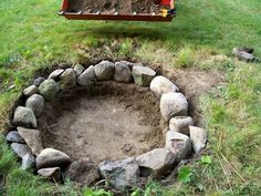 a circular stone fire pit in the middle of some grass and rocks on the ground