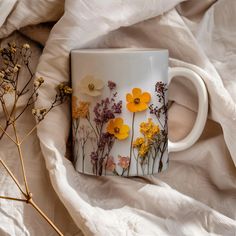 a white coffee mug with yellow and purple flowers painted on the side sitting on a bed