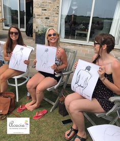 three women sitting on lawn chairs holding up drawings with their faces drawn in the same direction