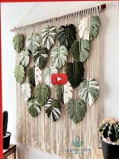 a wall hanging with green and white leaves on it next to a potted plant