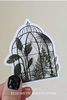 a hand holding up a sticker with an image of a birdcage