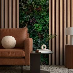 a brown chair sitting next to a table with a lamp on it and a green wall behind it