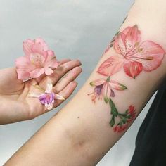 a woman holding out her arm with pink flowers on it and another flower in the other hand