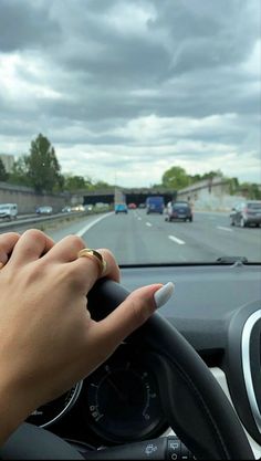 a person is driving on the road with their hand on the steering wheel and cars in the background