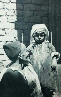 an old black and white photo of a woman in costume talking to a man wearing a headdress