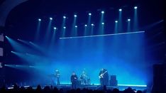 a group of people that are standing on a stage with lights in the dark behind them