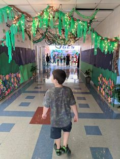 a young boy walking down a hallway decorated with green streamers and hanging decorations on the ceiling