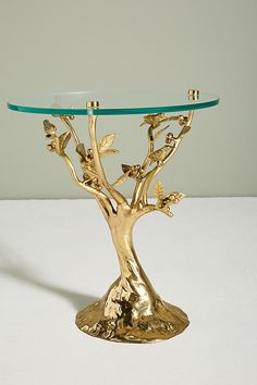 a gold tree table with glass top on a white surface in front of a gray wall