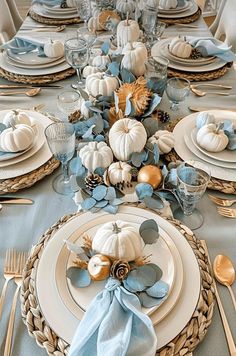 the table is set with blue and white dishes, silverware, and pumpkins