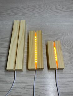 three pieces of wood with lights attached to them on a wooden surface, one is plugged in and the other two are turned yellow