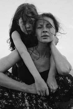 two women sitting on the ground with their arms around each other, one holding her head