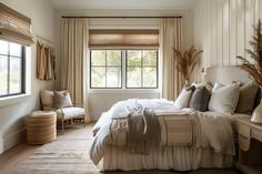 a bed sitting under a window in a bedroom next to a chair and ottomans