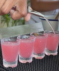 a person is pouring pink liquid into small glasses