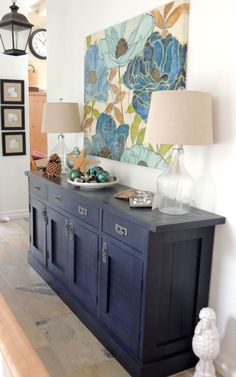 a blue buffet table with two lamps and a painting on the wall in the background