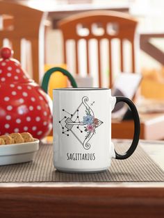 a white coffee mug sitting on top of a table next to a bowl of cookies