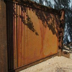 an old rusted metal fence with trees casting a shadow on it's side