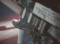 a close up of an electric guitar with a sign on it's neck that says, vandalism beautiful as a rock intopop space