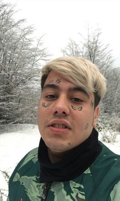 a man with tattoos on his face standing in front of snow covered trees and bushes