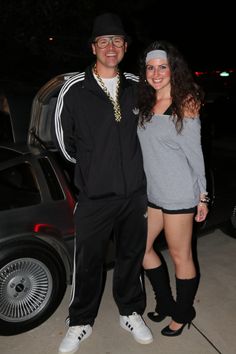 a man and woman standing next to each other in front of a car at night