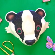 a cow mask sitting on top of a green table next to scissors and flowers with butterflies around it