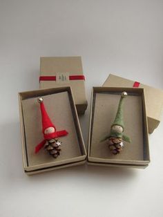 two small christmas ornaments in boxes on a table next to one another with an elf's hat and pine cone