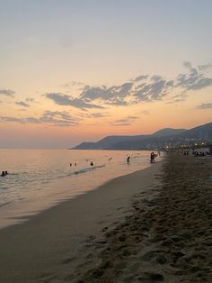 people are walking on the beach at sunset