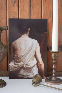 a white candle sitting next to a painting on top of a table