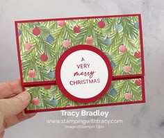 a hand holding up a christmas card with pine branches and berries on it, in front of a marble background