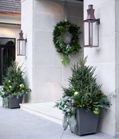 two potted plants sitting next to each other on the side of a building with wreaths