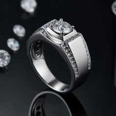 a white gold ring with diamonds surrounding it on a black surface surrounded by other jewelry items