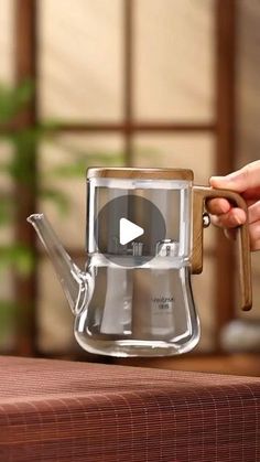 a person holding a wooden handle over a glass coffee pot with a video playing on it