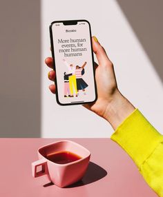 a person holding up a cell phone next to a cup of tea on a pink table