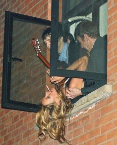 a woman holding a guitar up to her face while standing next to a brick building