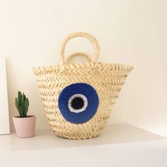 Straw Evil Eye Small Bag: Stylish Protection in a Compact Design Embrace a blend of fashion and function with the Straw Evil Eye Small Bag. This unique accessory is not just a stylish addition to your wardrobe but also a symbol of protection. Handcrafted with care, this bag is designed to ward off negativity while carrying your essentials in style. Handcrafted Quality and Ethical Sourcing At the heart of the Straw Evil Eye Small Bag is a commitment to quality and sustainability. Each bag is meticulously crafted by skilled artisans using natural materials sourced from Morocco. The use of traditional weaving techniques ensures that every bag is unique and durable, making it a timeless piece you can rely on. The Protective Power of the Evil Eye The centerpiece of this small bag is the strikin Crochet Table Mat, Handcrafted Accessories, Traditional Weaving, Dress Hats, Pet Bed, Compact Design, Small Bag, Weaving Techniques, Accessories Unique