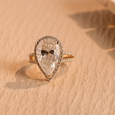 an engagement ring with a pear shaped diamond in the center on top of sand dunes