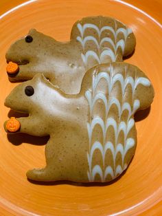 two cookies shaped like animals sitting on top of a yellow plate with orange and white decorations