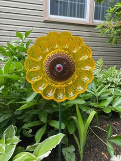 a yellow flower sitting on top of a lush green plant next to a building and bushes