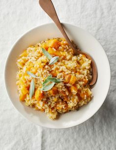 a white bowl filled with rice and vegetables next to a wooden spoon on top of a table