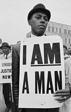 a man holding a sign that says i am a man in front of other people