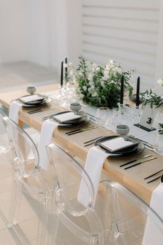 the table is set with clear chairs and place settings