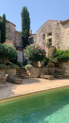 an outdoor patio with tables and chairs next to a pool in front of a stone building