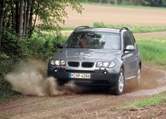 a silver car driving down a dirt road next to green grass and tree's