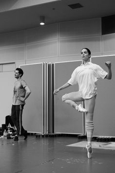 a woman is standing on one leg in the middle of a dance class while another man watches