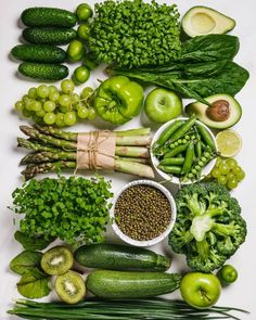 an assortment of fruits and vegetables on a white surface with green beans, broccoli, cucumbers, peas, apples, as well as well