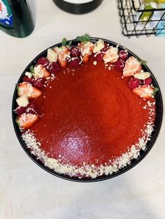 a red dessert with strawberries and other toppings in a black bowl on a white table