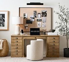 a desk with two chairs and a tree in the corner next to some pictures on the wall