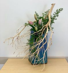 a blue vase filled with lots of different types of flowers and branches on top of a wooden table